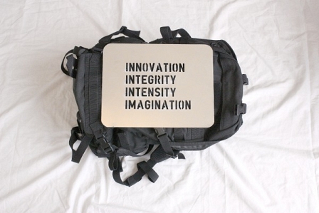 Metalplatte mit Aufschrift "Innovation - Integrity - Intensity - Imagination" liegt auf einem Rucksack